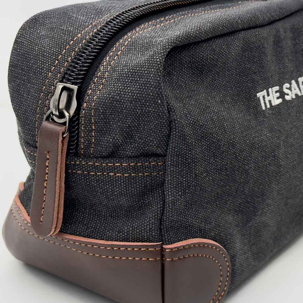 Black toiletry bag with brown zipper and leather accents on a light gray background