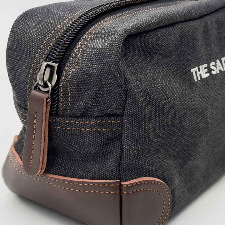 Black toiletry bag with brown zipper and leather accents on a light gray background